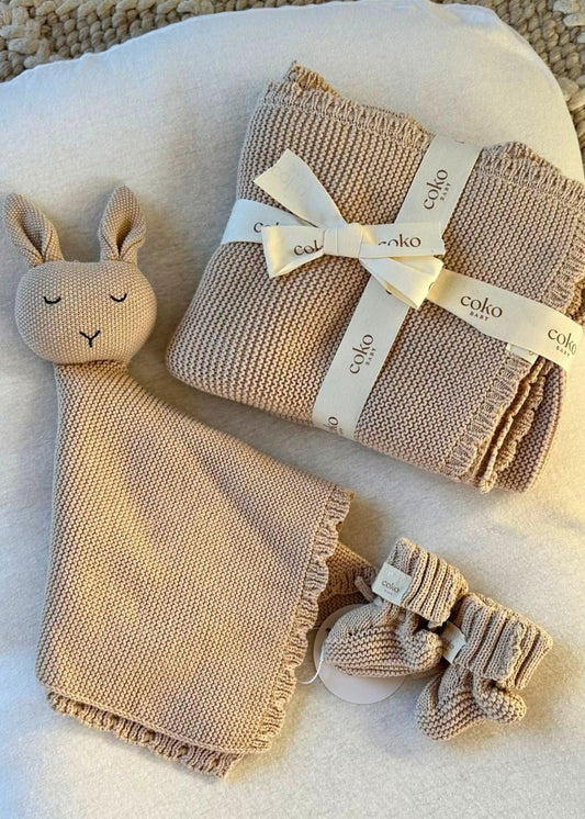 Baby gift set with brown knitted blanket, toy, and booties on a white surface