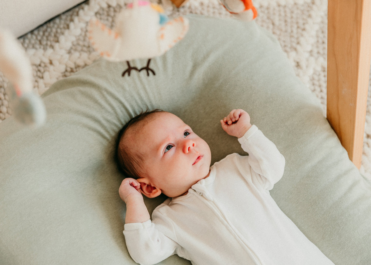 Baby lying on a green cushion with toys in the background